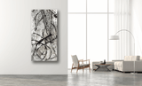 Tall vertical abstract canvas with black and gray ink and wax patterns featuring circular and linear shapes, displayed on a white wall beside modern seating and large windows.