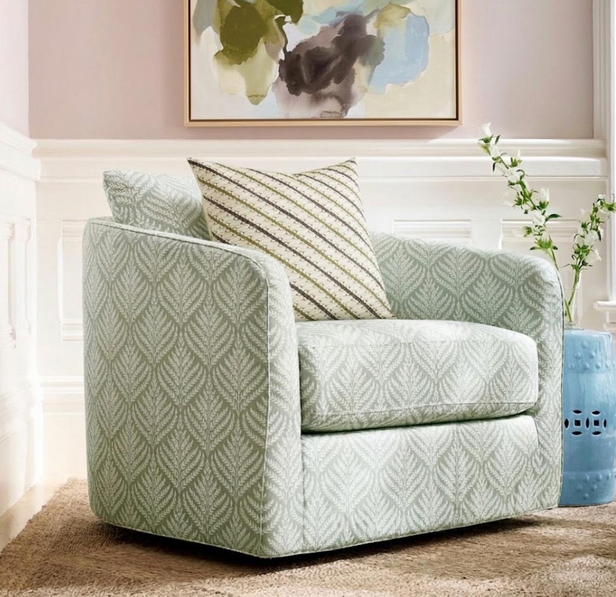 Light green armchair with a subtle leafy pattern paired with a square cushion featuring green and cream diagonal stripes, set on a beige rug near a blue ceramic stool.