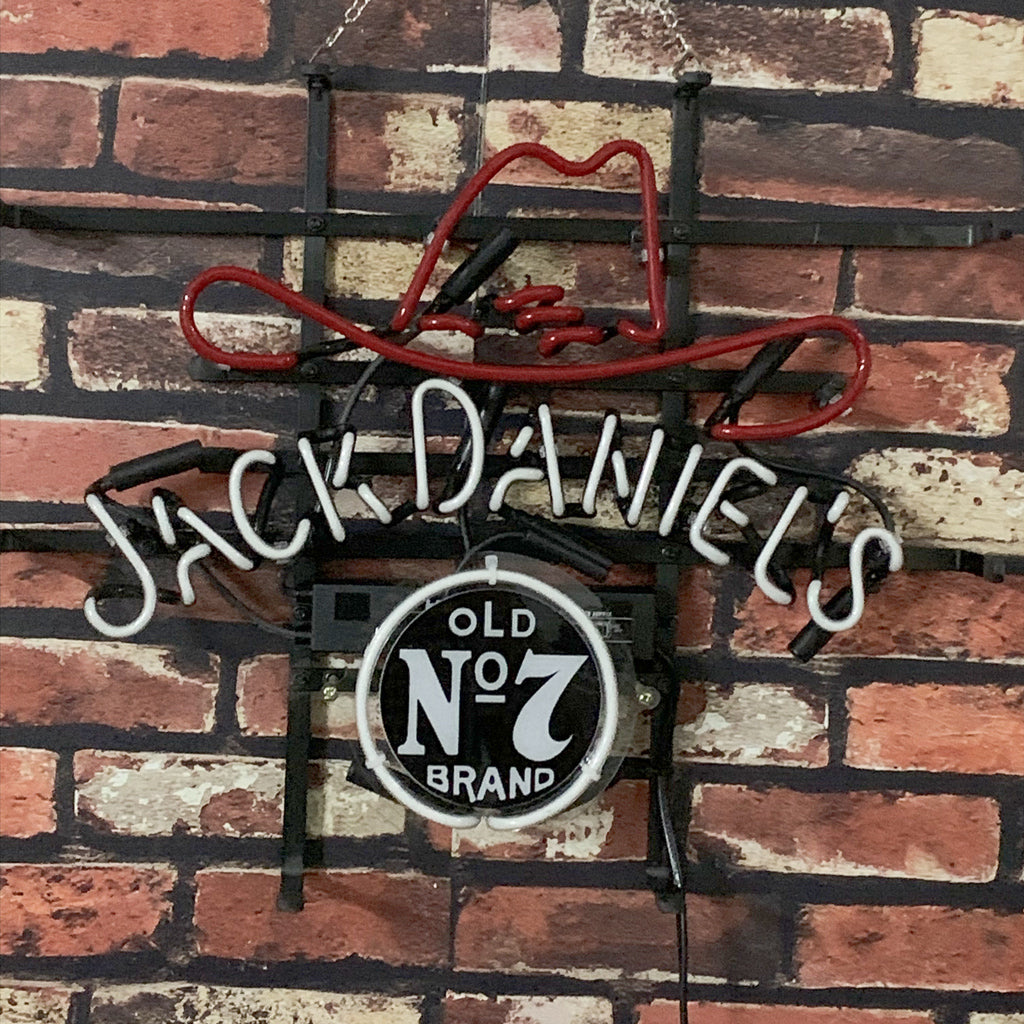 Neon sign featuring a red outlined cowboy hat and the text 'Jack Daniel's' in white, with a circular black and white 'Old No 7 Brand' emblem below, mounted on a brick wall.