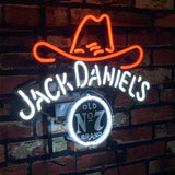 Neon sign with a red cowboy hat above white glowing 'Jack Daniel's' text and a circular black and white 'Old No 7 Brand' emblem, mounted on a brick wall.