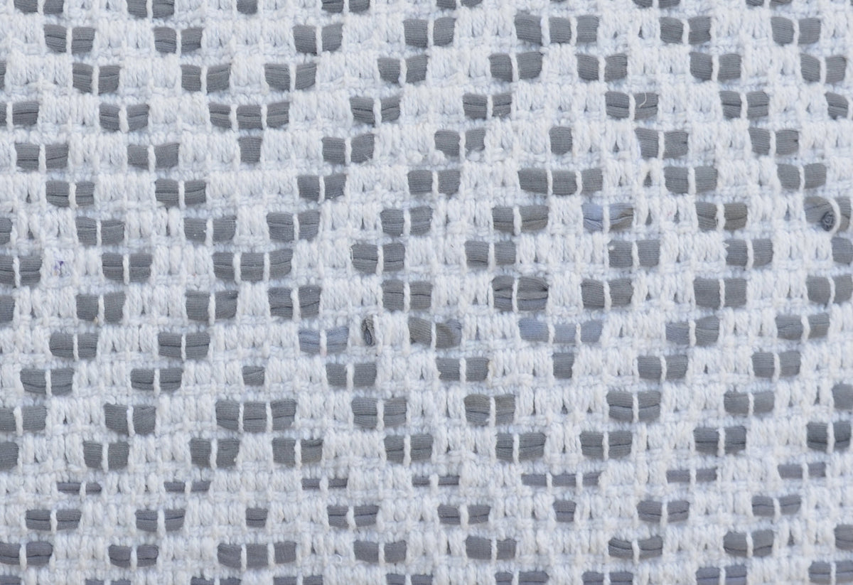 Close-up of a woven cotton textile with geometric diamond patterns in white and light grey shades, featuring a textured grid-like weave.