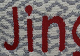 Close-up of a textured cushion cover showing the word 'Jingle' in bold red letters against a background of gray and white woven loops.
