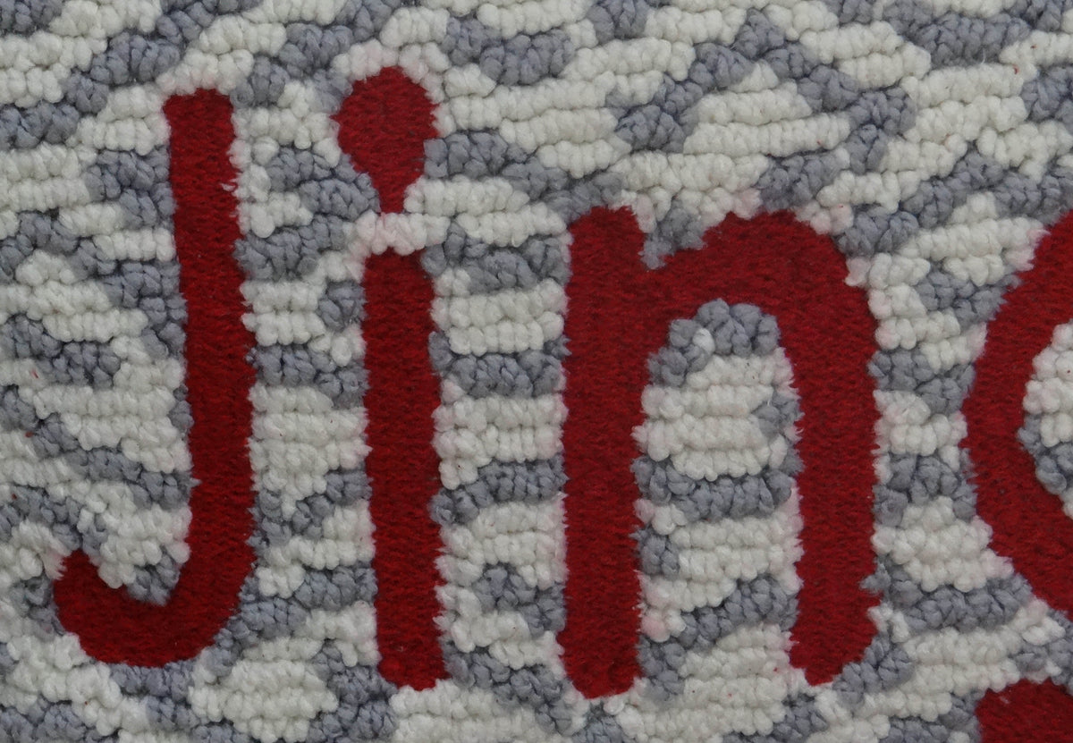 Close-up of a textured cushion cover showing the word 'Jingle' in bold red letters against a background of gray and white woven loops.