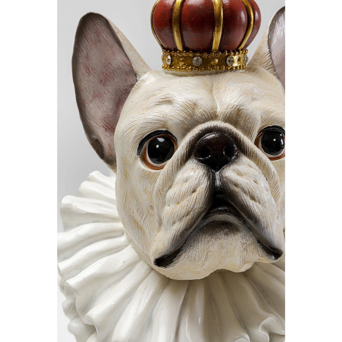 Close-up of a white bulldog figurine wearing a red and gold crown and a textured white ruffled collar, showing detailed facial features with large eyes and wrinkled skin.