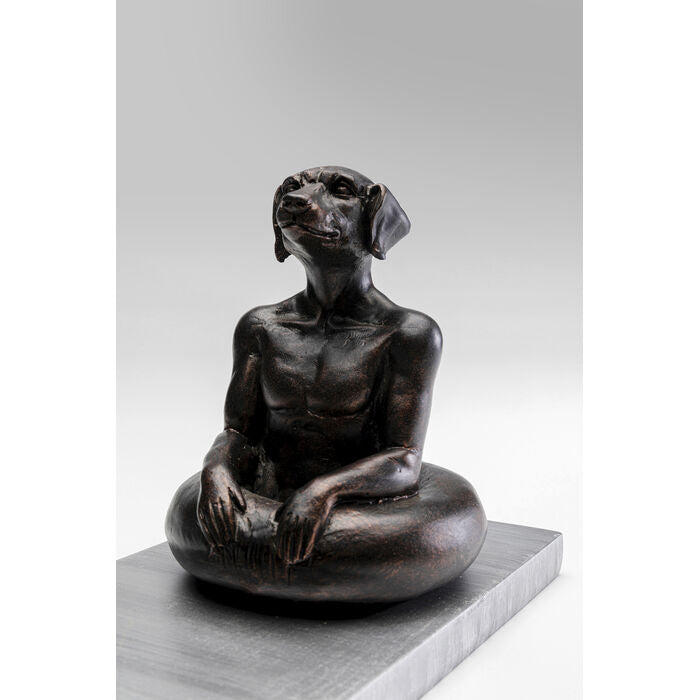 Dark bronze sculpture of a dog-headed human figure sitting cross-legged on a square base, with detailed muscular torso and relaxed hands resting on knees.