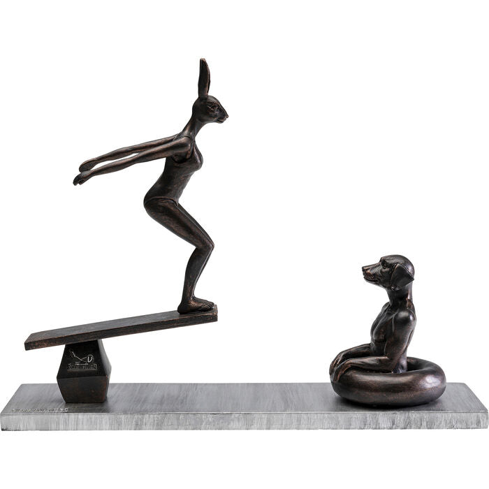 Dark bronze figurine of a humanoid rabbit poised on a seesaw opposite a seated humanoid dog, mounted on a rectangular gray base.