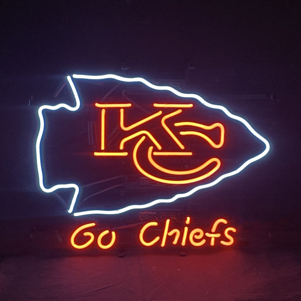 Neon sign featuring a white arrowhead outline with red interlocking KC letters inside and orange text saying 'Go Chiefs' below on a dark background.
