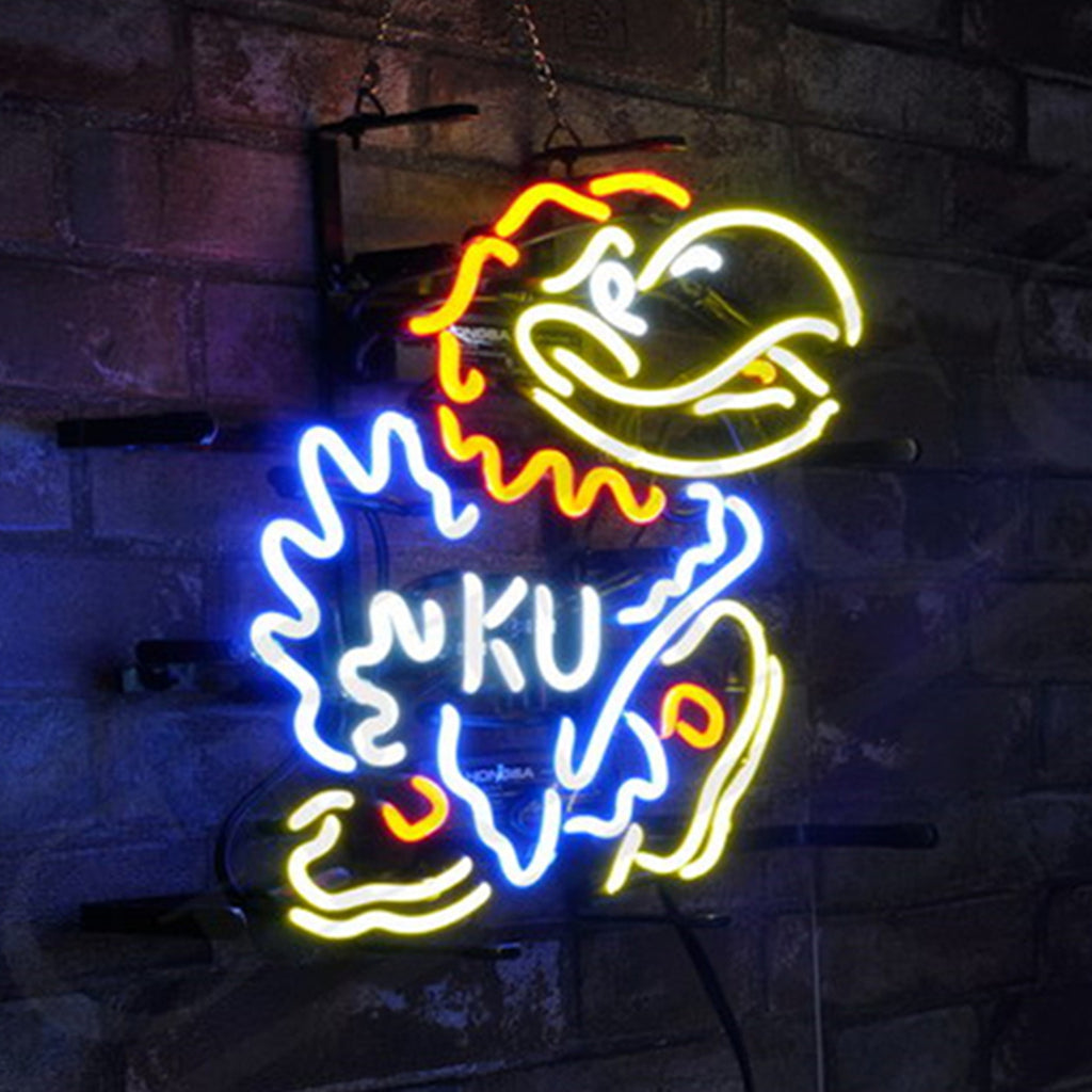 Neon sign of a blue, yellow, and red Jayhawk mascot with 'KU' in white on its chest, mounted on a dark brick wall and glowing brightly.
