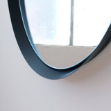 Close-up of a round mirror with a smooth, matte black frame reflecting a window with white panes and soft natural light.