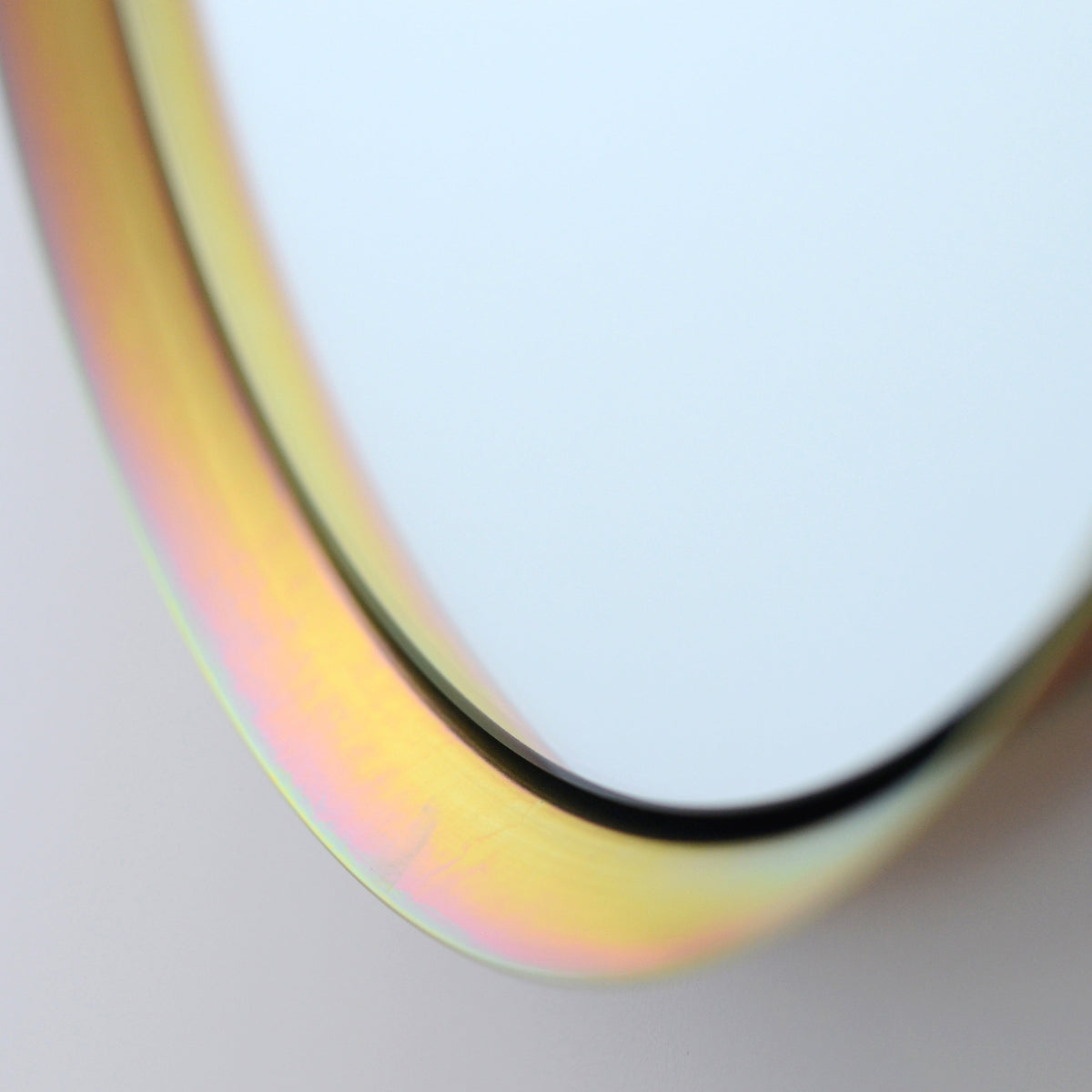 Close-up of a round mirror with a smooth metallic frame reflecting soft iridescent yellow and pink hues against a neutral background.