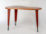 Kidney-shaped wooden desk with warm brown top and tapered reddish-brown legs ending in slender black metal tips, shown against a white background.