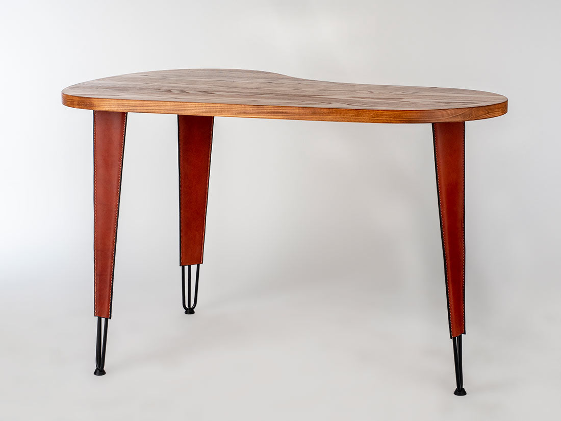 Kidney-shaped wooden desk with warm brown top and tapered reddish-brown legs ending in slender black metal tips, shown against a white background.