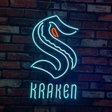 Neon light sign showing stylized blue 'S' shaped Kraken logo with an orange eye detail above the word KRAKEN in blue neon, mounted on a red brick wall.