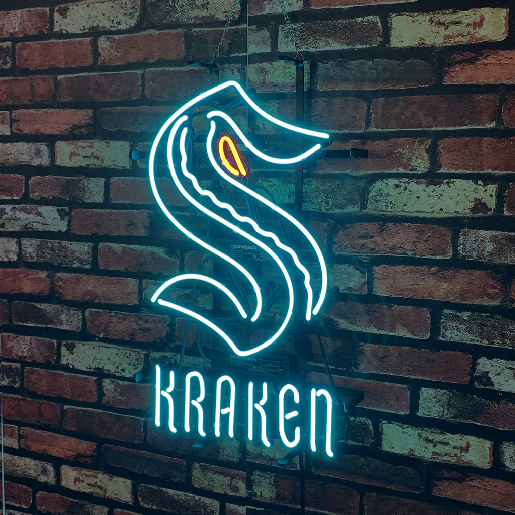 Bright blue neon sign in the shape of an 'S' with an orange eye detail, above glowing blue text spelling 'KRAKEN', mounted on a red brick wall.