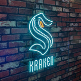 Neon light sign shaped like a stylized sea creature with a prominent orange eye and the word 'KRAKEN' in bright blue below, mounted on a red brick wall.