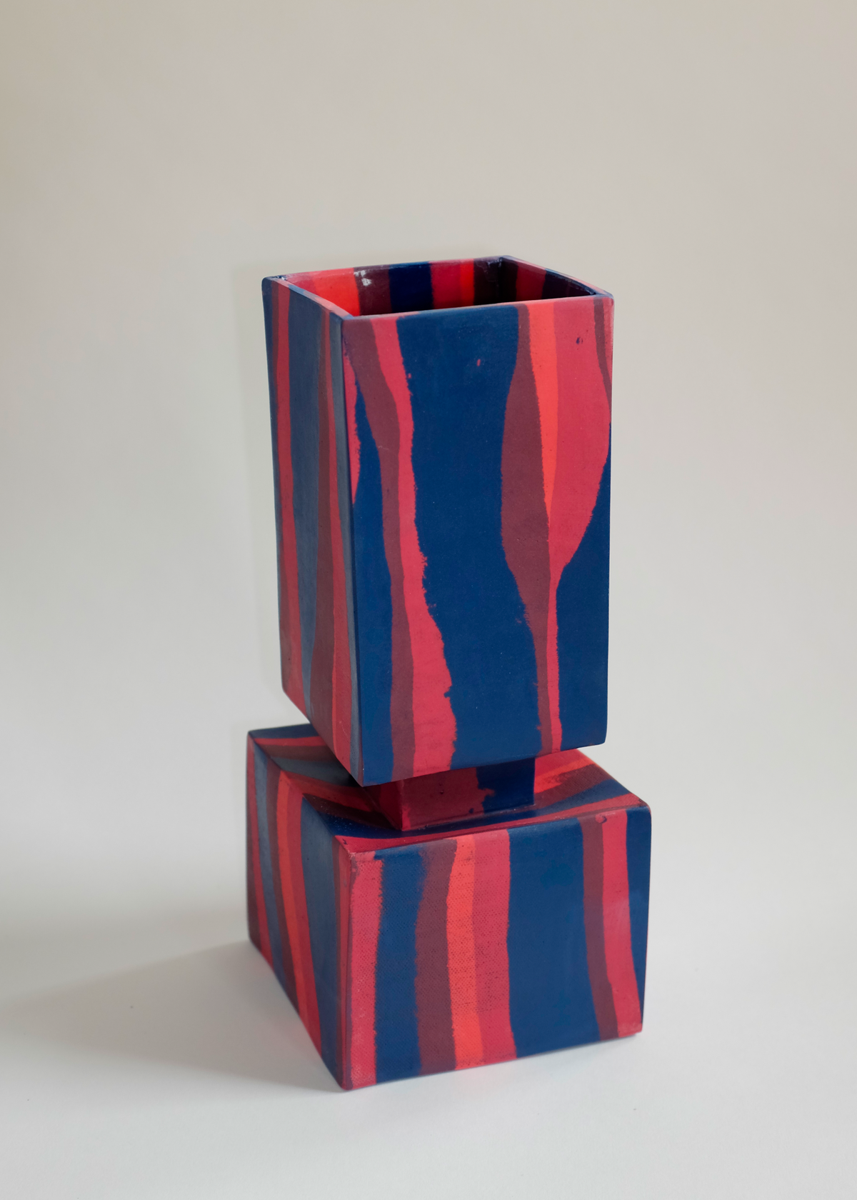 Squared vase composed of two stacked cubes with vertical and horizontal red and navy blue marbled stripes, displayed against a neutral background.