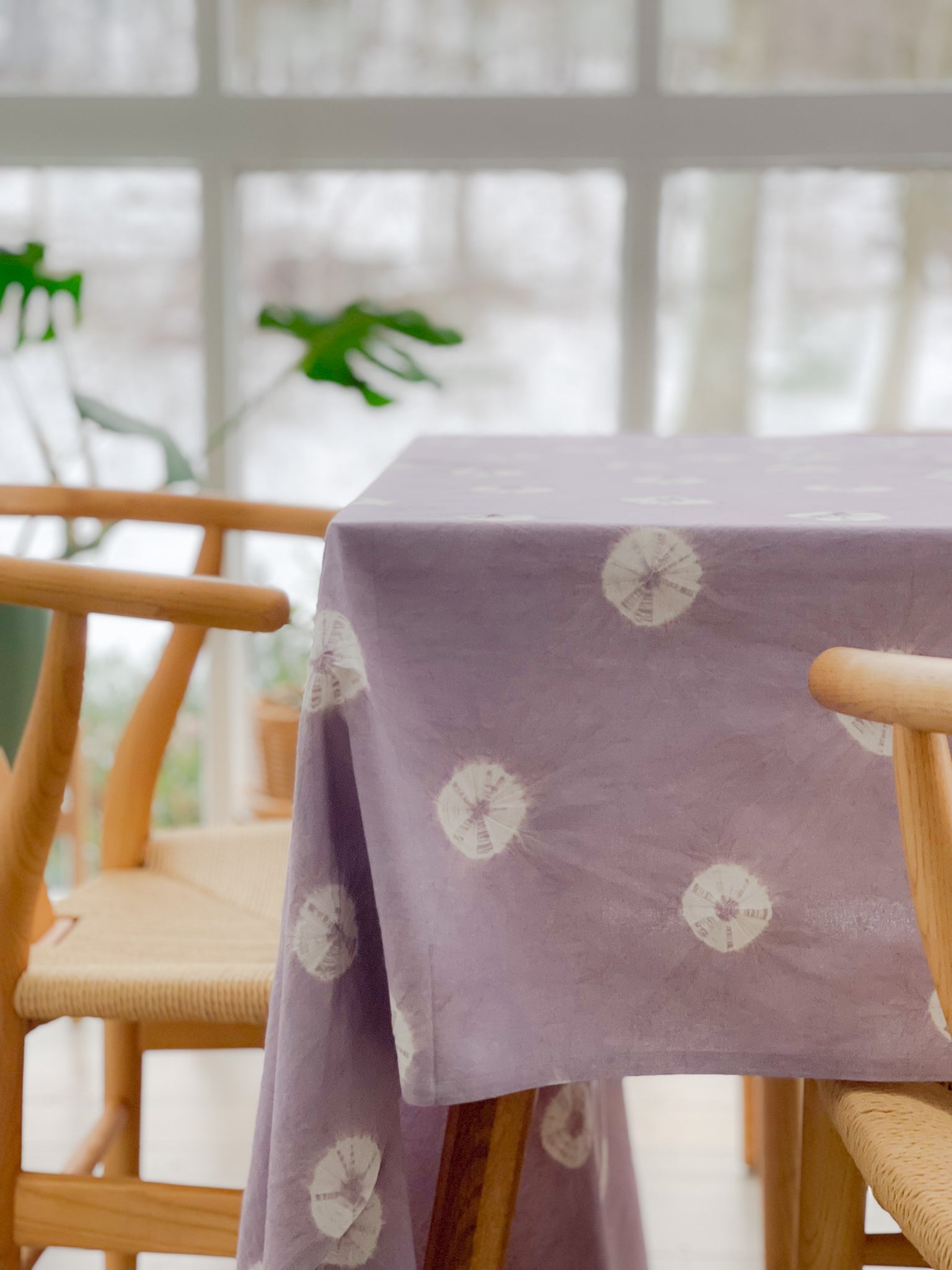 Shibori Tablecloth in dusky lavender draped over a dining table with a simple setting