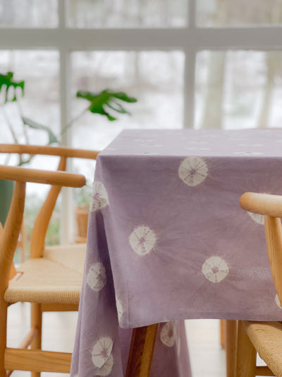 Shibori Tablecloth in dusky lavender draped over a dining table with a simple setting