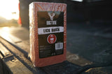 Rectangular reddish cherry-scented lick brick with Bigtine branding, placed on a textured black surface with warm sunlight in the background.