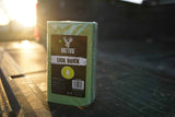 Green rectangular block labeled 'BIGTINE LICK BRICK' standing upright on a dark wooden surface with sunlight shining from the background.