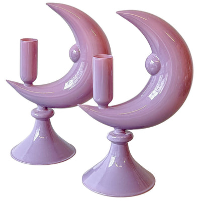 Pair of lilac glass candle holders shaped like crescent moons on a white surface