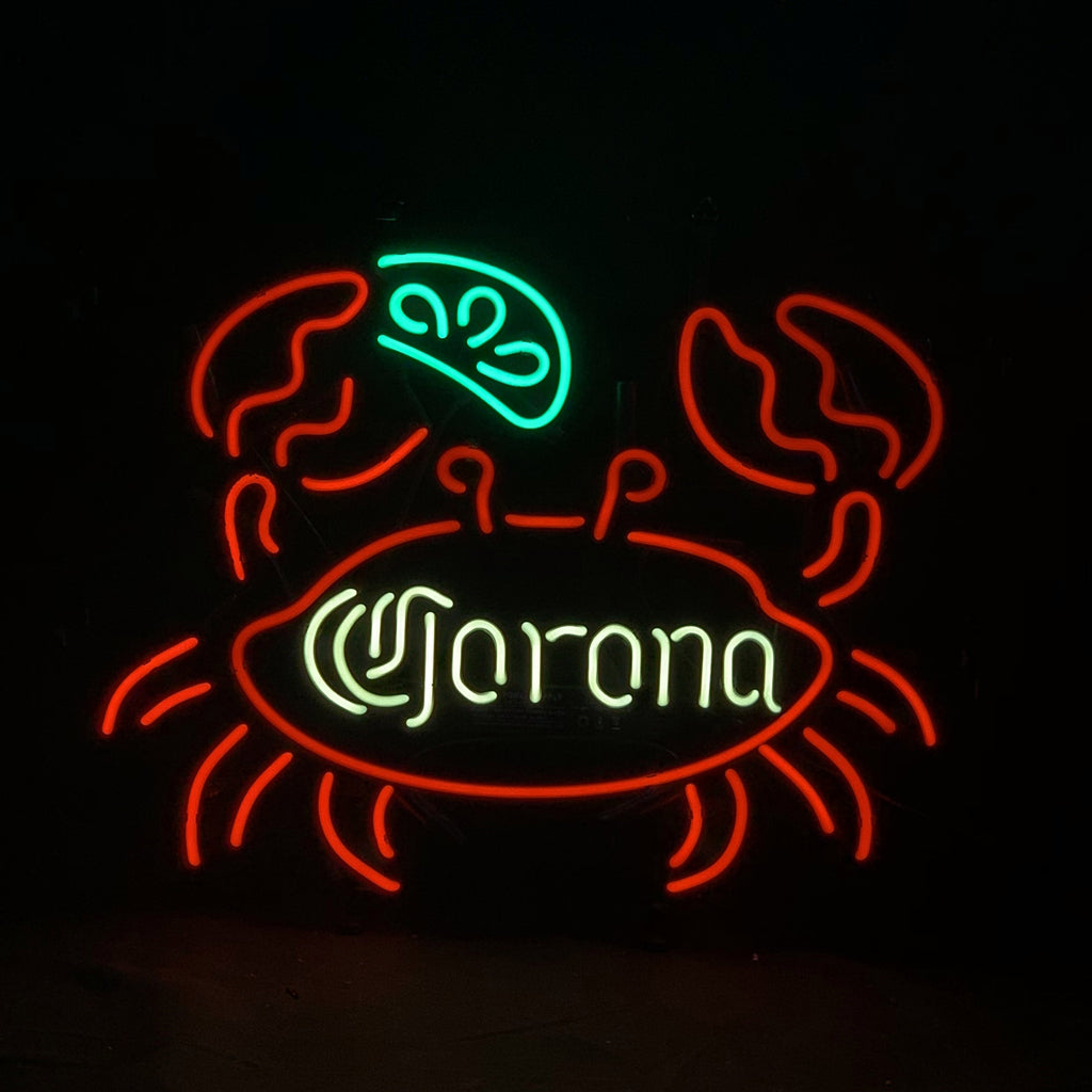 Neon sign shaped like a red crab holding a green lime wedge above white 'Corona' text inside its body on a black background.
