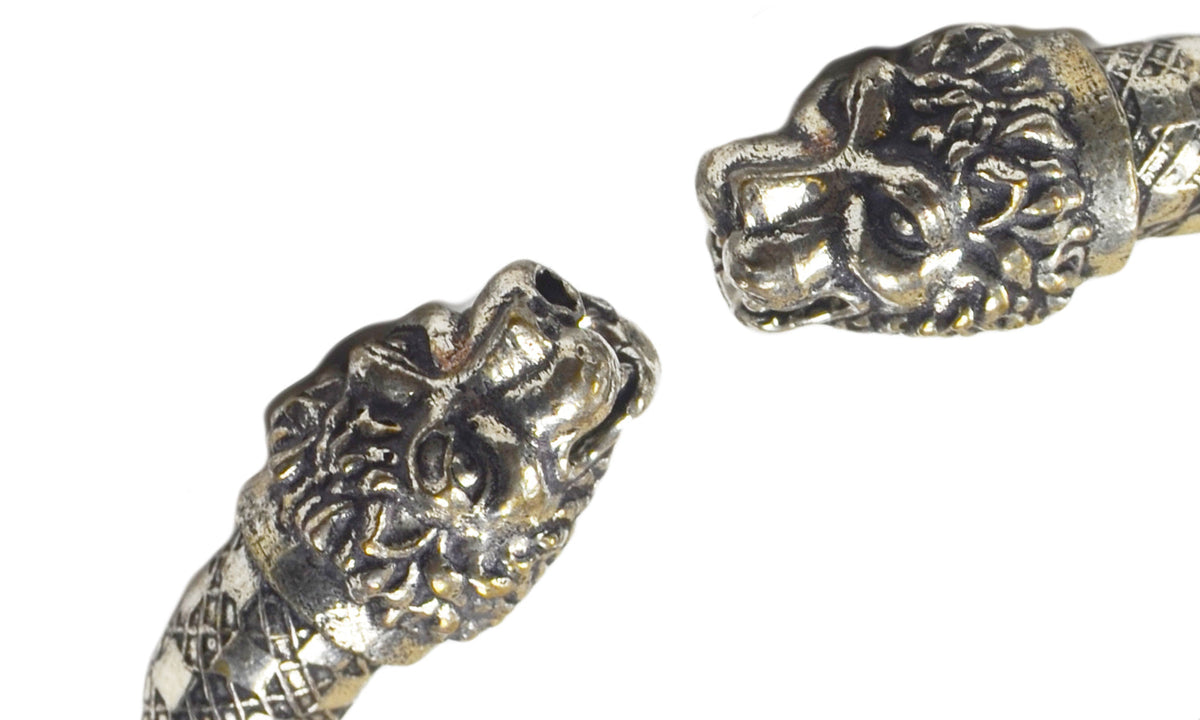 Close-up of an antique-style Viking bracelet with detailed lion head terminals and a woven square pattern on the band, shown on a white background.