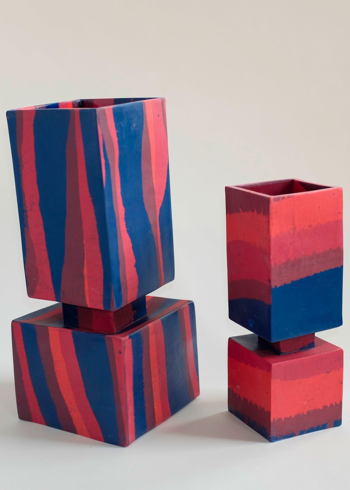 Two squared vases with a modern design, featuring bold vertical and horizontal stripes in blue and reddish-pink hues, each with a stacked square base and top section.