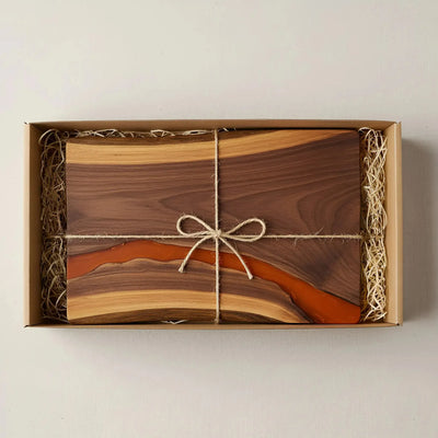 Live edge black walnut charcuterie board with matte burnt orange epoxy resin river and matte black metal handles, ready for serving.