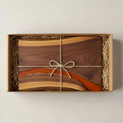 a charcuterie board carefully packaged for shipping. The board is made from live edge black walnut with a smooth, polished finish and a matte burnt orange epoxy river running through the center. It’s wrapped in kraft paper and tied neatly with natural twine for a handmade, artisan feel. Matte black metal handles are attached at both ends.