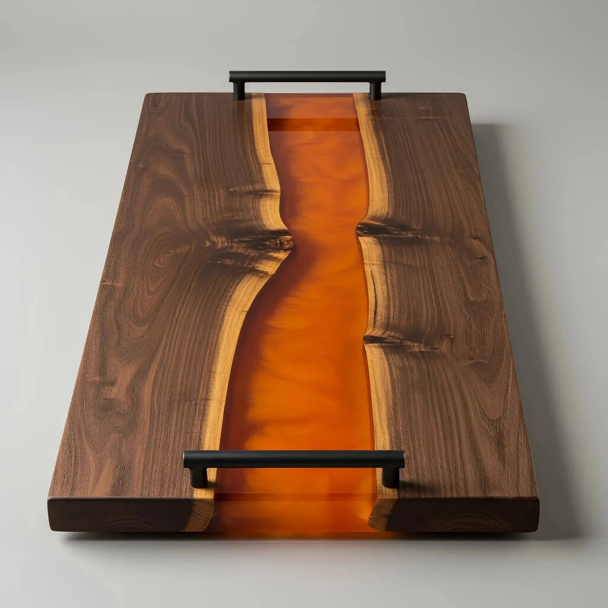 charcuterie board, 18 inches by 9 inches, made from live edge black walnut wood with a deep, glossy orange epoxy river flowing through the center. The resin has a rich, translucent amber or burnt orange tone that contrasts beautifully with the dark walnut grain. The board features a smooth, polished finish and matte black metal handles at each end.