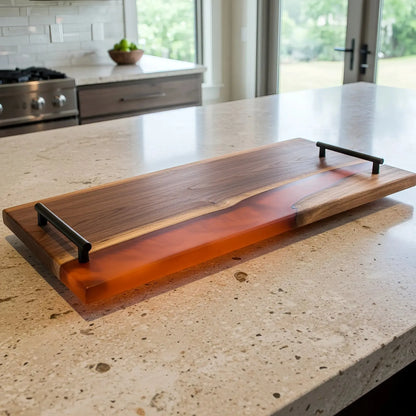 charcuterie board, 18 inches by 9 inches, made from live edge black walnut wood with a matte burnt orange epoxy river running through the center. The resin is warm and earthy—like amber or terracotta—with a subtle, non-glossy finish and soft texture. Matte black metal handles are attached at each end with a top bar that extends slightly past the posts.