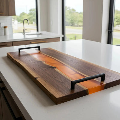 Live edge black walnut charcuterie board with matte burnt orange epoxy resin river and matte black metal handles, ready for serving.