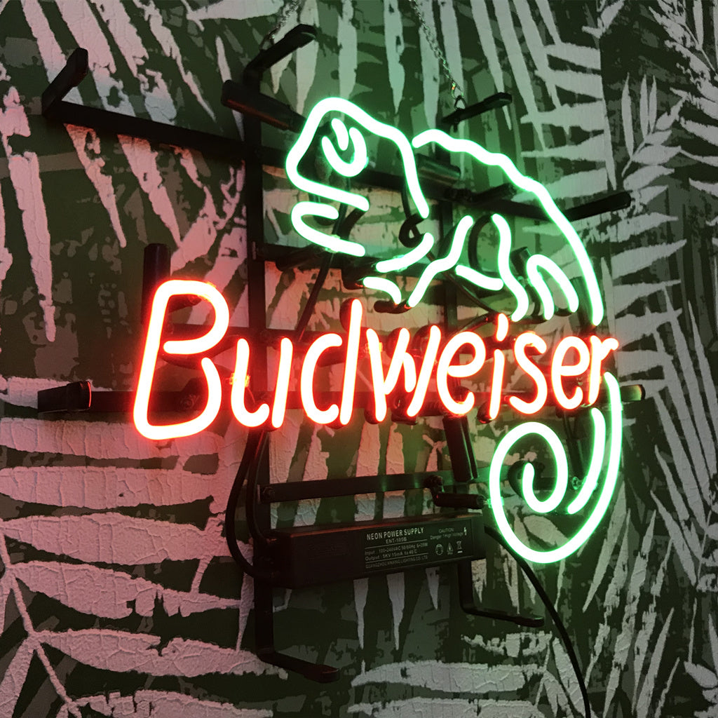 Neon sign with red Budweiser text and a green lizard outline mounted on a black leafy patterned wall.