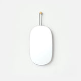 Minimalist oval mirror with rounded edges hanging on a white wall by a thin black strap attached to a small wooden peg.