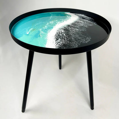 Round resin table with a black rim and legs, featuring a design of ocean waves on the top.