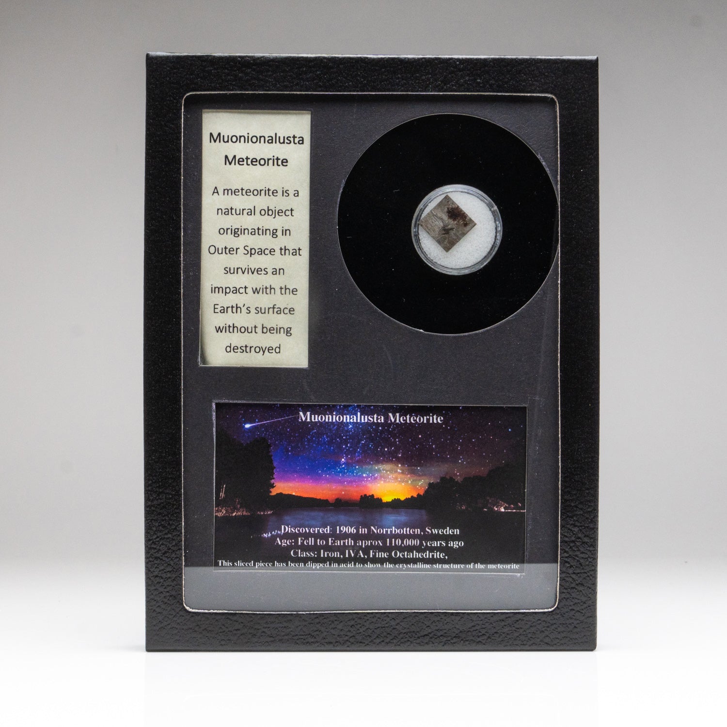 Genuine Muonionalusta Meteorite fragment displayed in a glass box with label and image.