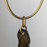 Close-up of Macrya Necklace pendant with a dark green, irregular-shaped resin piece hanging from two bronze-colored rings on a textured golden cord.