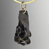 Glossy black abstract pendant with curving, folded shapes hanging from a thin beige cord against a soft gray background