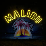 Bright yellow neon letters spelling 'MALIBU' arch over a colorful sign featuring two silhouetted palm trees against a purple and orange sunset background on a dark wall.