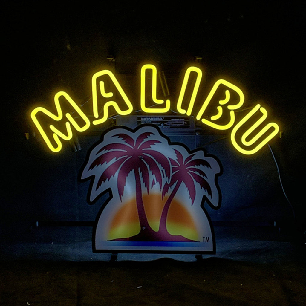 Bright yellow neon letters spelling 'MALIBU' arch over a colorful sign featuring two silhouetted palm trees against a purple and orange sunset background on a dark wall.