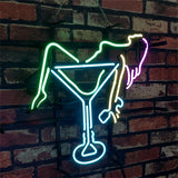 Neon sign of a figure lounging inside a turquoise martini glass with neon yellow, green, and pink outlining against a brick wall background.