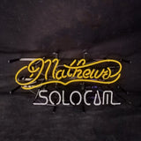 Yellow cursive neon sign reading 'Mathews' above white block letters spelling 'SOLOCUM' against a dark background.