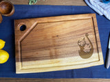 Medium live edge wooden cutting board with a juice groove, angled square end, a round hanging hole, and a deer and hook silhouette engraved design.