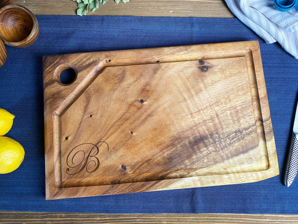 Medium rectangular live edge cutting board with a juice groove, hanging hole at one corner, and engraved letter B on the wood surface.