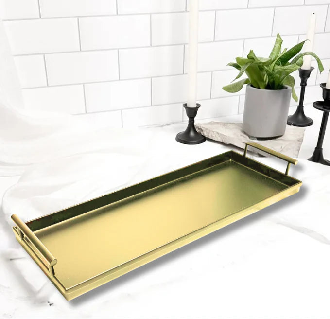 Gold tray on a white surface with decorative elements like a plant and candles.