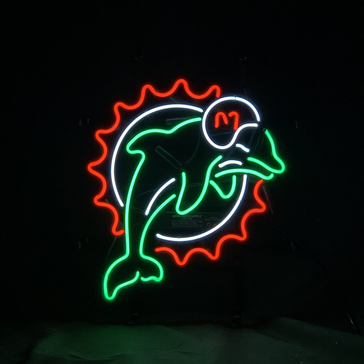 Neon sign of a green dolphin wearing a white helmet with an orange 'M,' encircled by a white ring and an orange sunburst pattern.