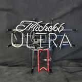 White neon script spelling 'Michelob' and block letters 'ULTRA' with a red neon outline below, mounted on black metal and wiring against a dark background.