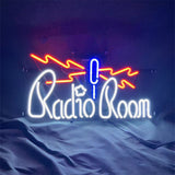Neon sign with white cursive 'Radio Room' text, a blue vertical microphone shape in the center, and red zigzag lines above on a dark background.