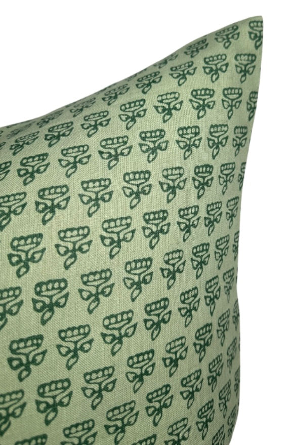 Close-up of a green pillow cover patterned with small, repeating dark green stylized floral motifs arranged in neat rows on a muted green background.